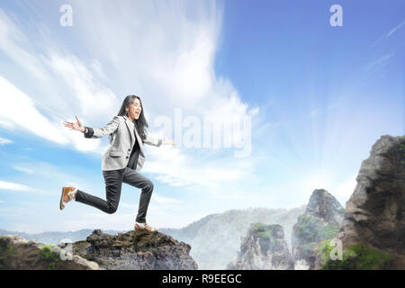 Young Asian business woman in costume formel de sauter sur le sommet de la montagne. Concept d'entreprise réussie Banque D'Images