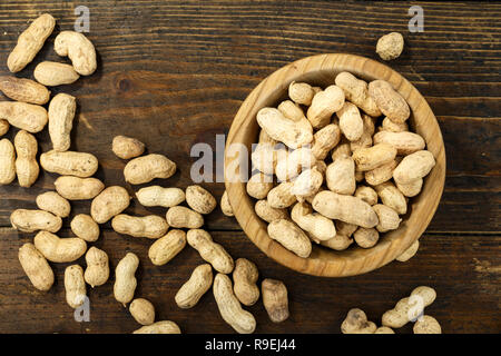 Arachides décortiquées dans une assiette et d'arachides dans un peel sur un fond de bois. traditionnel café snack. Un espace réservé au texte Banque D'Images