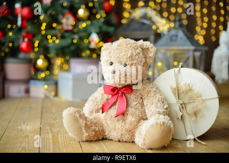 Les nounours de l'emplacement sous l'arbre de Noël avec des cadeaux. Maison de l'arrière-plan. Lumières de Noël Banque D'Images