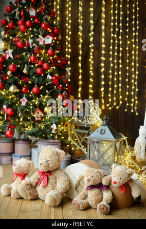 Famille d'ours de l'emplacement sous l'arbre de Noël avec des cadeaux. Maison de l'arrière-plan. Lumières de Noël Banque D'Images