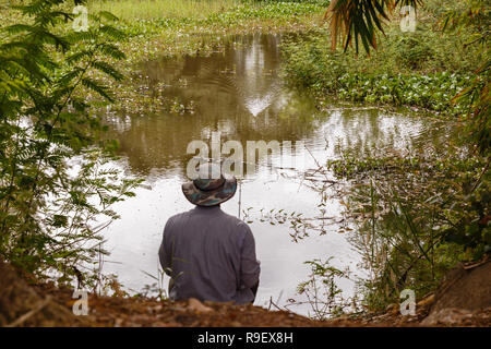 Homme dans un chapeau jette une canne à pêche sur un petit étang Banque D'Images