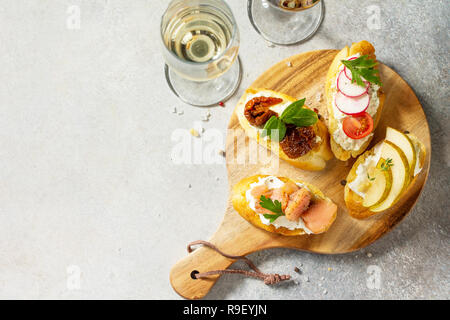 Antipasti italiens des en-cas pour le vin. Brushetta avec fromage, poire, radis, le saumon et les tomates séchées sur un fond noir en lumière. Vue supérieure de la télévision Banque D'Images