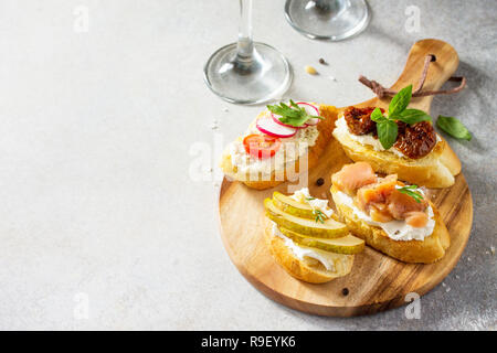 Antipasti italiens des en-cas pour le vin. Brushetta avec fromage, poire, radis, le saumon et les tomates séchées sur un fond noir en lumière. Copier l'espace. Banque D'Images