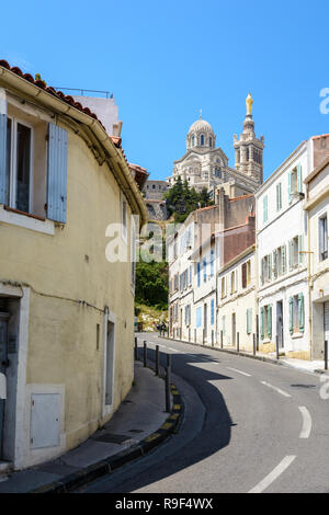 Une étroite rue en pente bordée de maisons anciennes à Marseille, France, allant jusqu'à Notre-Dame de la garde en haut de la colline. Banque D'Images