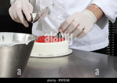 Mains pâtissier prépare un gâteau, couvrir avec du glaçage et décorer avec des fraises, travaille sur un travail de cuisine industriel en acier inoxydable haut Banque D'Images
