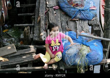 Une petite fille assise sur une terrasse en bois dans un village de pêcheurs au Cambodge Banque D'Images