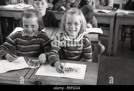 Années 1950, historiques, des enfants de l'école primaire, école secondaire Langbourne, England, UK. Photo montre deux jeune filles- peut-être des soeurs jumelles comme ils se ressemblent et portent des cavaliers identiques - assis à côté de l'autre, à un bureau à deux places en bois faire une classe d'art. Banque D'Images