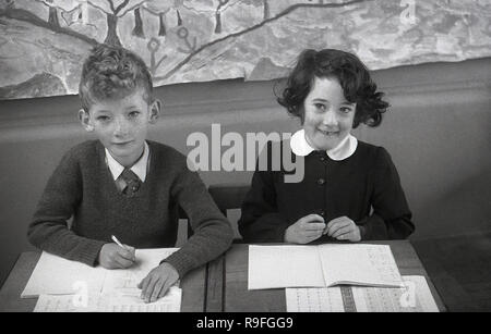 Années 1950, historiques, des enfants de l'école primaire, école secondaire Langbourne, England, UK. Photo montre un jeune garçon et fille assise à côté de l'autre, à un à deux places, l'école en bois 24 avec leur travail en classe. Banque D'Images