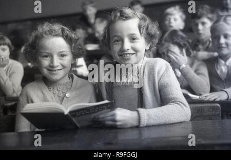 Années 1950, historiques, des enfants de l'école primaire, école secondaire Langbourne, England, UK. Photo montre deux jeune filles, peut-être des soeurs jumelles comme ils ont l'air très semblables, assis à côté de l'autre, à un bureau avec un livre ouvert. Banque D'Images