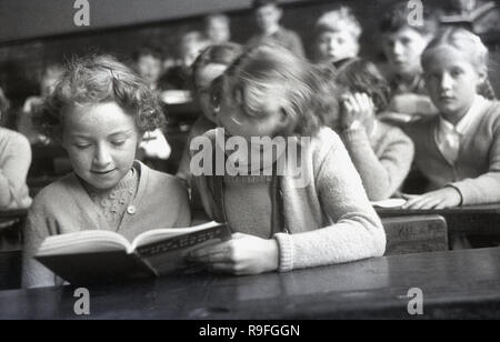 Années 1950, historiques, des enfants de l'école primaire, école secondaire Langbourne, England, UK. Photo montre deux jeunes filles assis à côté de l'autre, à un bureau en bois, le partage d'un livre. Banque D'Images