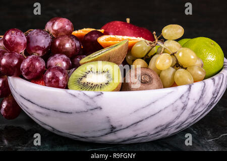 Panier de fruitson tropicaux frais dans un bol sur le noir en arrière-plan. L'ananas, papaye, mangue, kiwi, raisin, grenat, mandarines, bananes, pommes, wate Banque D'Images