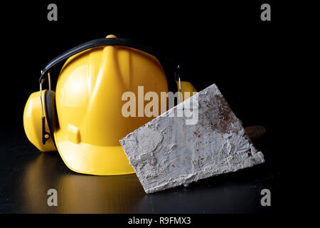 Outils pour maçon et casque sur un tableau noir. Accessoires pour les travailleurs de la construction. Fond sombre. Banque D'Images