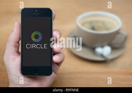 Un homme se penche sur son iPhone qui affiche le logo du cercle (usage éditorial uniquement). Banque D'Images