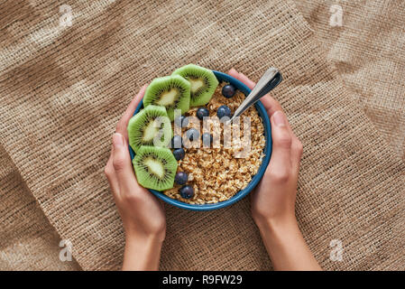 La vitamine le petit-déjeuner. Vue de dessus de céréales de petit-déjeuner sain avec des baies, graines de citrouille, de l'avoine et les kiwis dans un bol sur l'isolé. Femme heands sont holding. Banque D'Images