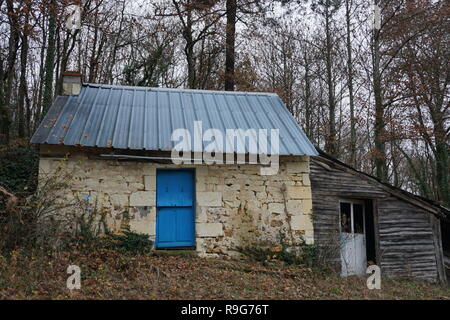 Porte bleu vif sur une ancienne petite maison en pierre et hangar en bois dans les bois dans le pays en France Banque D'Images