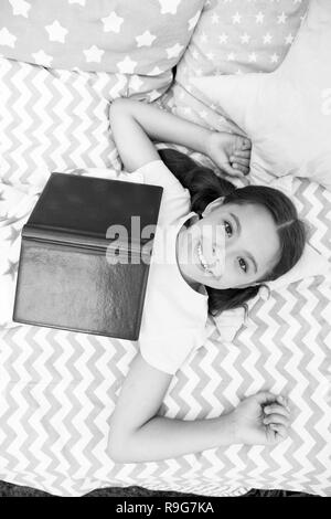 Lit enfant fille lay read book vue d'en haut. Kid se préparer à aller au lit. Temps agréable dans une chambre confortable. Kid fille cheveux longs pyjamas mignons vous détendre et lire livre. Encourager les habitudes utiles. Satisfait de professionnels. Banque D'Images