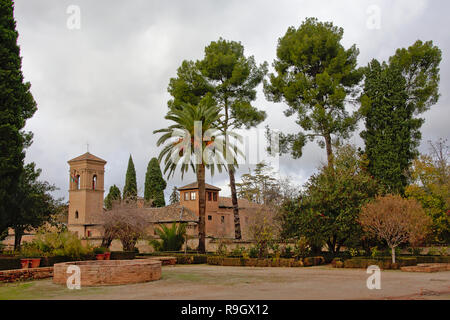 Patio avec tour de l'horloge et de palmiers et de cyprès sur un jour nuageux à Alhambra, Granada, Espagne Banque D'Images