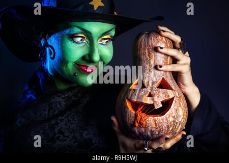 Sorcière avec peau verte tenue Halloween citrouille sculptée au fond sombre Banque D'Images