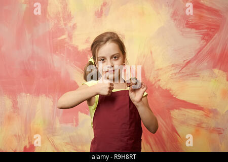 Enfant giving Thumbs up geste pour gâteau. L'alimentation saine et l'alimentation de concept. Girl with cupcake. La Boulangerie et boulangerie délicieuse. Baby cook en tablier chef rouge sur colourful abstract wall. Banque D'Images