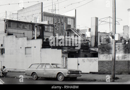 Lithgow, Australie 1977 : une vue latérale de rue de l'arrière des bureaux et des magasins montrant un désordre confus de construction. Au premier plan, un homme s'accroupe près du caniveau et un break Ford Falcon XR est stationné directement devant un panneau No parking. Banque D'Images