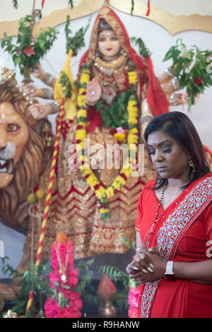 Une pieuse femme hindoue dans un sari rouge prier et méditer devant une statue de Durga dans un temple en Jamaïque, Queens, New York. Banque D'Images