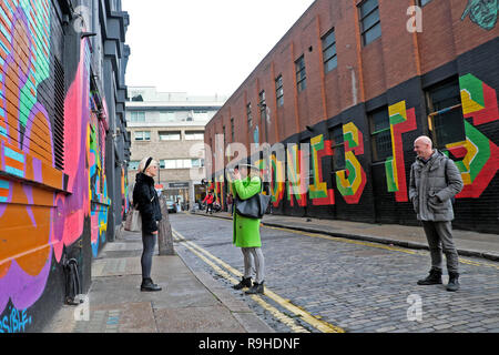 Une femme photographe dans la région de lime green coat photographier une jeune femme dans une rue avec des graffitis colorés à Shoreditch East London UK . KATHY DEWITT Banque D'Images