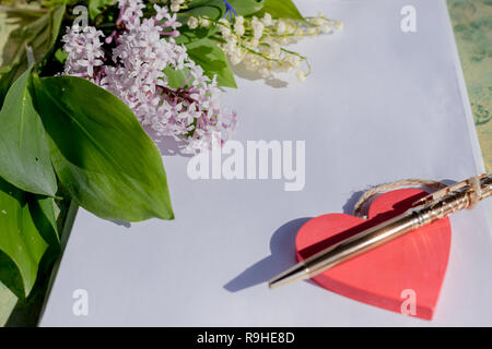 Lettre sur l'amour des maquettes en bois.Red Heart se trouve sur papier blanc vierge sur une table en bois avec fleurs de printemps, une carte de vœux pour le jour de Valentine avec une place pour votre texte. Mise à plat, de lilas et de lys de la vallée. design pour la Saint-Valentin Banque D'Images