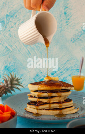 Pile de crêpes verser marple syrup. Petite verseuse dans une main d'homme. Le petit-déjeuner. Jem, papaye. Vue de côté Stock photo Banque D'Images