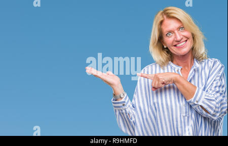 L'âge moyen d'affaires blonde femme de plus fond isolé surpris et souriant à la caméra tout en présentant avec la main et en pointant avec le doigt. Banque D'Images