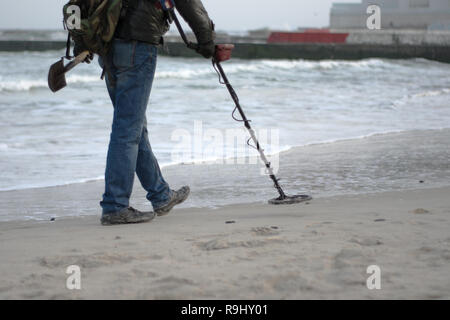 Homme avec détecteur de métal sur la plage à la recherche d'objets perdus sous le sable de l'océan, sur la mer. Digger noir. Hunter pour pièces, l'or, de l'antiquité. Banque D'Images