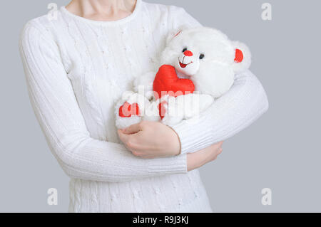 La jeune fille est titulaire d'un ours blanc avec un cœur dans ses mains. Fond gris. Banque D'Images