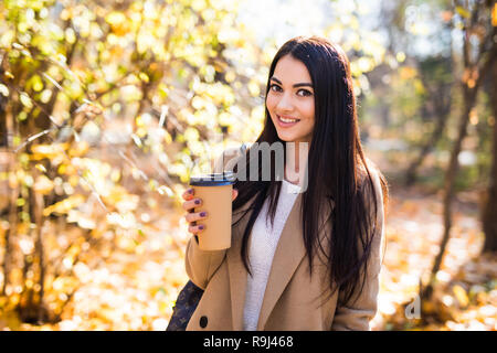 Jeune femme marche dans la rue de la ville d'automne et de boire du café à emporter dans la tasse de papier. Banque D'Images