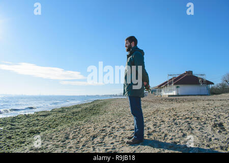 Un beau jeune homme pensif, avec une barbe se tient sur la mer et se penche sur la distance. rêver guy sur l'arrière-plan de la mer jour ensoleillé. Banque D'Images