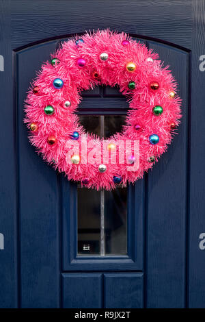 Couronne de Noël rose fluorescent avec décoration de Noël sur un chalet bleu porte avant dans Deddington, Oxfordshire, Angleterre Banque D'Images