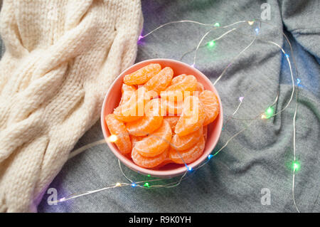 Mise à plat de Rose bowl full of sweet tangerines pelées sur fond gris avec guirlande lumières. Banque D'Images