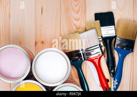 Quatre pots de peinture avec des pinceaux sur fond de bois naturel. Jaune, blanc, rose, turquoise couleurs. Concept de rénovation.