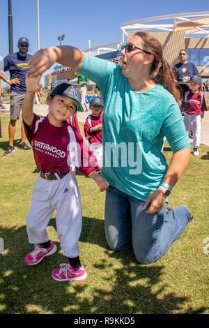Un portrait 4-year-old girl en uniforme de la petite ligue prend un tour de danse avec sa mère à un Irvine, CA, softball stadium. Banque D'Images