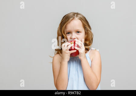 Portrait of a happy smiling little blonde sur un fond gris. Baby eating red apple Banque D'Images