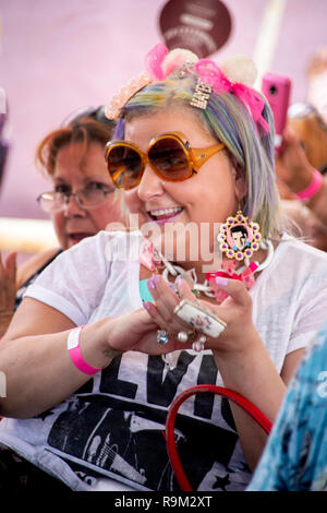 Une femme enthousiaste dans l'auditoire d'un emprunt d'Elvis Presley rock and roll music festival à Fullerton, CA, porte des photos d'Elvis dans ses boucles d'Elvis et un T shirt comme elle applaudit les interprètes. Banque D'Images