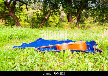 Guitare acoustique portant sur textile bleu plaid sur l'herbe Banque D'Images