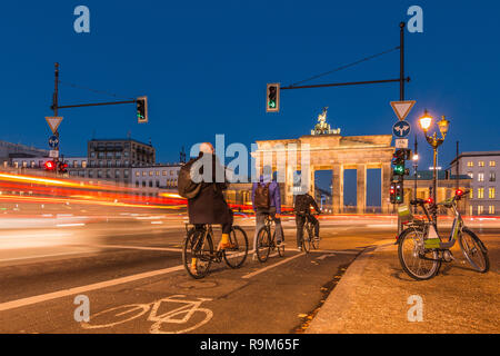 L'arrière de la porte de Brandebourg dans la nuit. Les cyclistes sont en attente au feu de circulation. voitures passant dans une exposition à long terme. Un e-bike est sur le bord de la route Banque D'Images