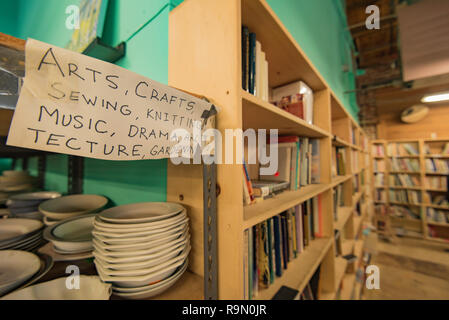 Un signe écrit à la main au-dessus de livres et de la vaisselle (assiettes) empilés sur des étagères dans un magasin d'épargne dans le Mission District de San Francisco, Californie, USA Banque D'Images