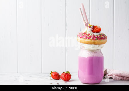 Fraise rose Freak Shake cocktail avec donut et des bonbons sur un fond blanc, l'espace de copie. Desserts malsain concept. Banque D'Images