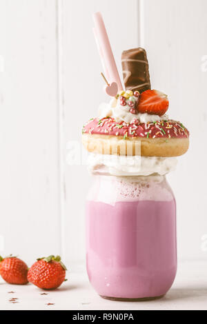 Fraise rose Freak Shake cocktail avec donut et des bonbons sur un fond blanc. Desserts malsain concept. Banque D'Images