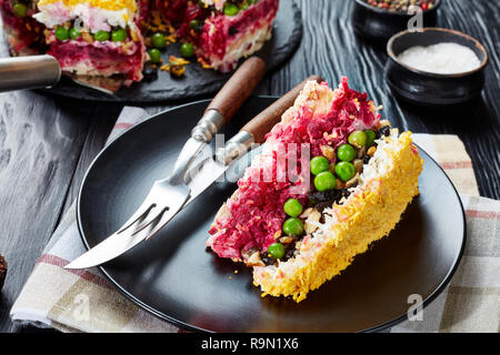 Close-up d'une tranche de gâteau en couches avec salade de légumes, œufs durs, les pruneaux, les noix hachées et la viande de poulet servi sur une plaque noire Banque D'Images