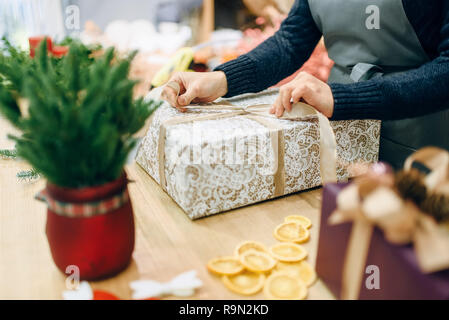 Personne de sexe féminin d'un archet sur des liens d'or boîte cadeau, fait main rétractable et la décoration. Femme wraps présent sur la table, le décor intérieur Banque D'Images