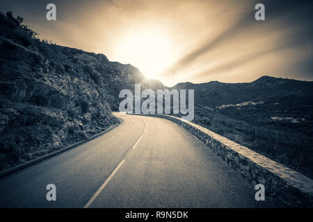 Image en noir et blanc à la recherche vers le coucher de soleil sur une route sinueuse dans les montagnes de la Balagne Corse Banque D'Images