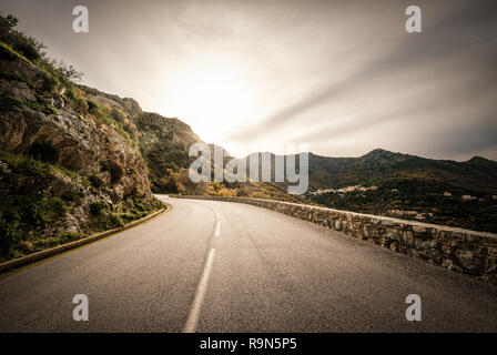 En regardant vers le coucher de soleil sur une route sinueuse dans les montagnes de la Balagne Corse Banque D'Images