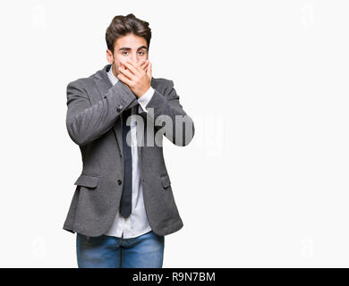 Entreprise jeune homme portant costume et cravate sur fond isolé choqué couvrant la bouche avec les mains pour l'erreur. Concept Secret. Banque D'Images