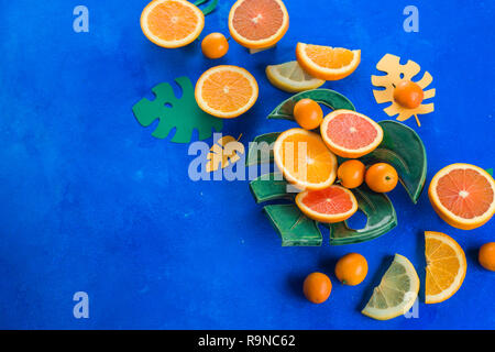 Mangues, oranges, kumquats et autres fruits tropicaux sur une plaque monstera. Fond bleu lumineux avec copie espace. En-tête d'aliments exotiques. Banque D'Images